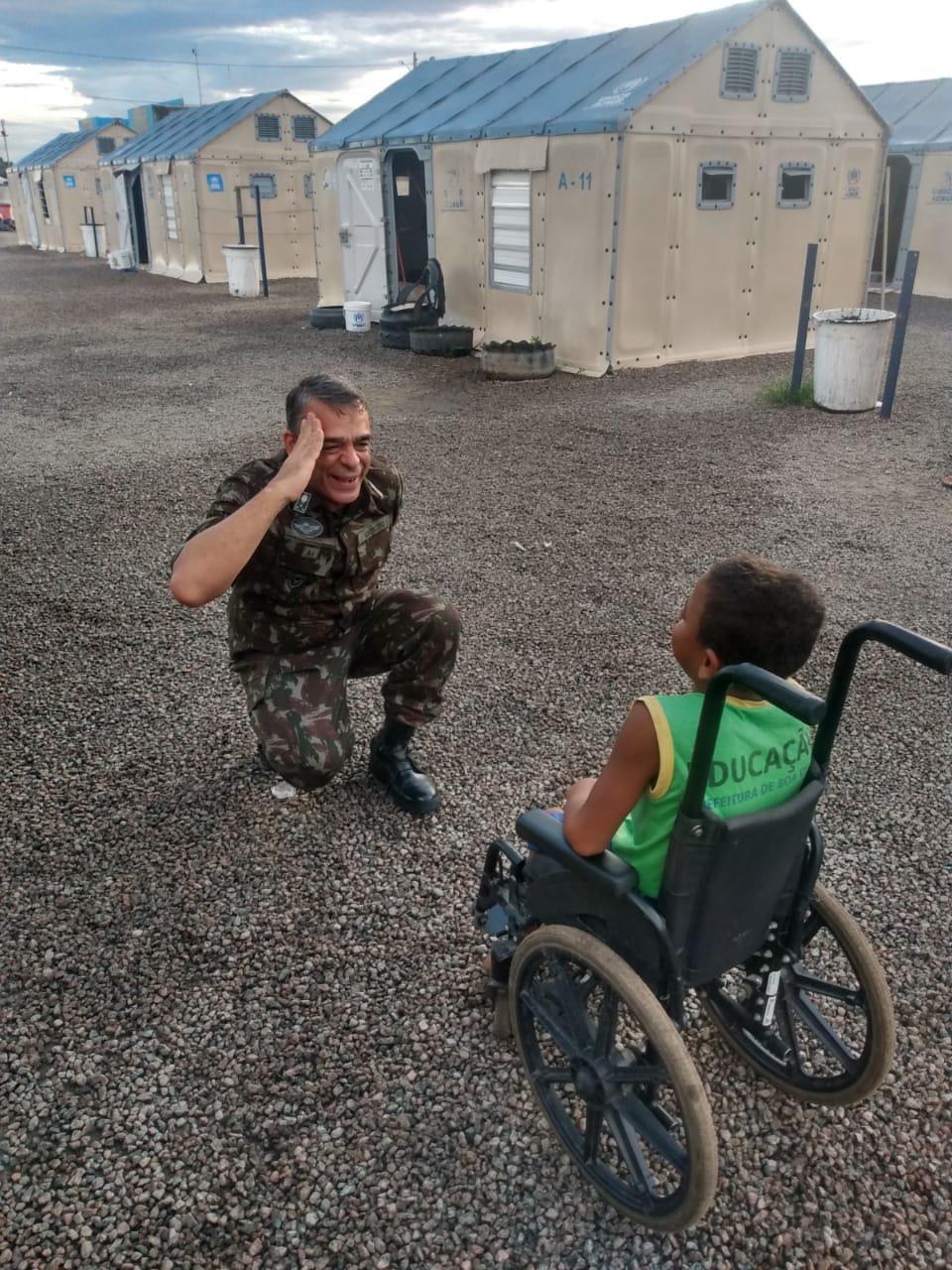 Militar interagindo com uma criança em cadeira de rodas durante a Operação Acolhida